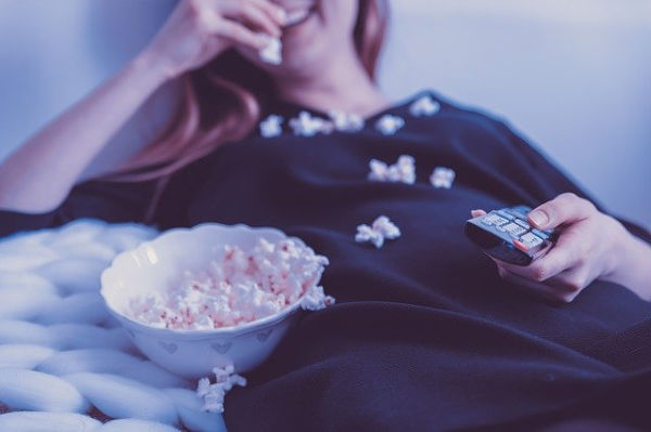 Woman eating popcorn and watching television.