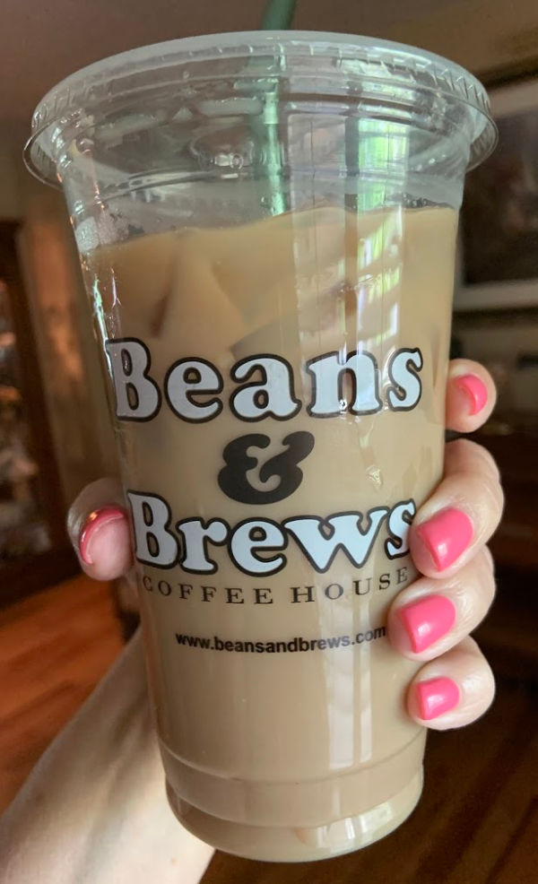Manicured hand holding a Beans and Brews latte.