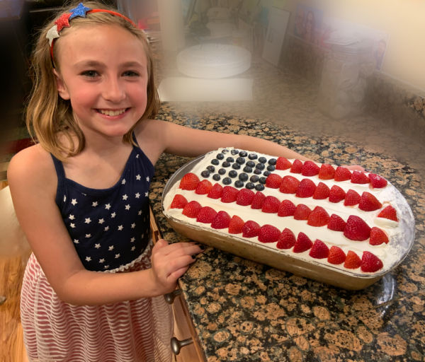 Young girl dressed in red, white, and blue holding a United States flag cake.