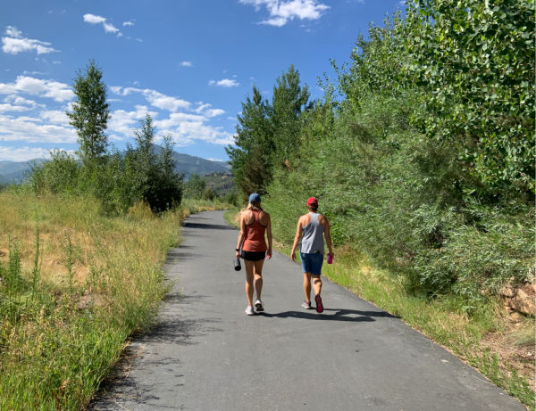 Two women walking tree-lined trail.