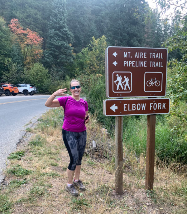 Woman standing next to the Pipeline to Elbow Fork Trail sign.