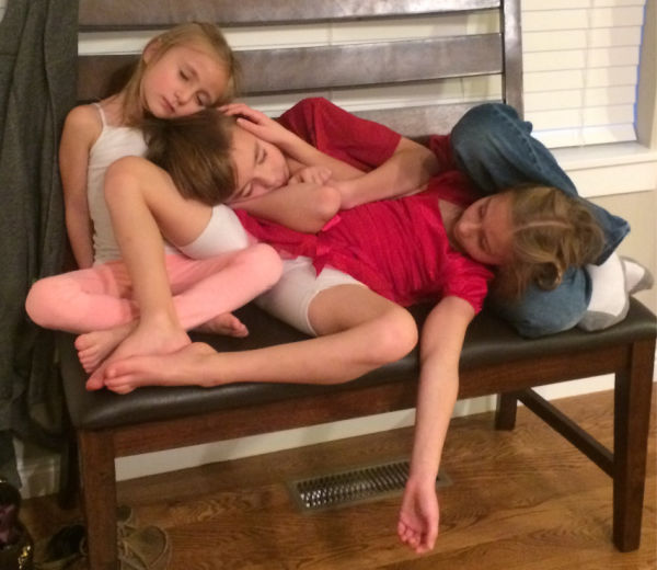 Three children sleeping in a pile on a bench.
