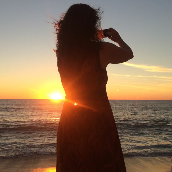 Woman taking photos of a sunset over the ocean.