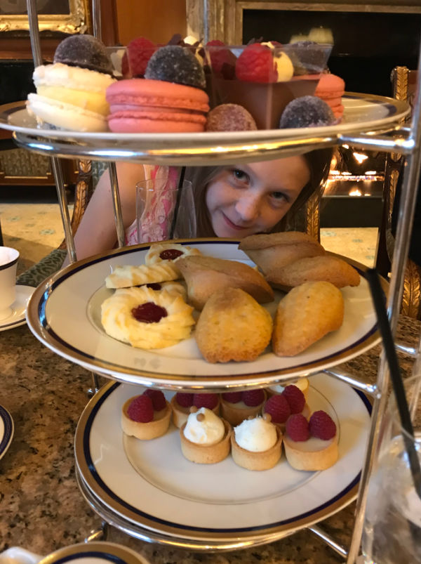 Girl peeking through a tray of pastries.