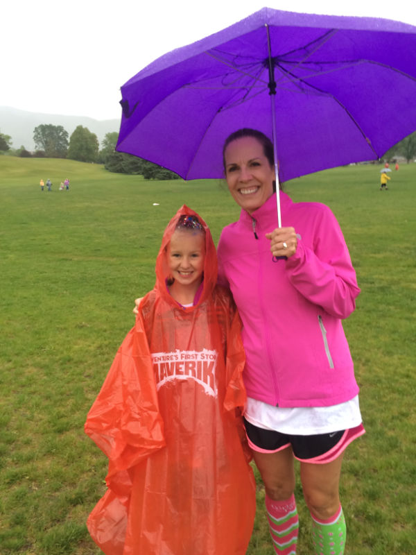 A lady and her granddaughter under an umbrella at a race.