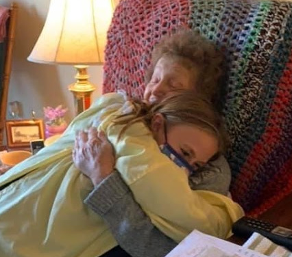 Girl in PPE hugging grandmother.