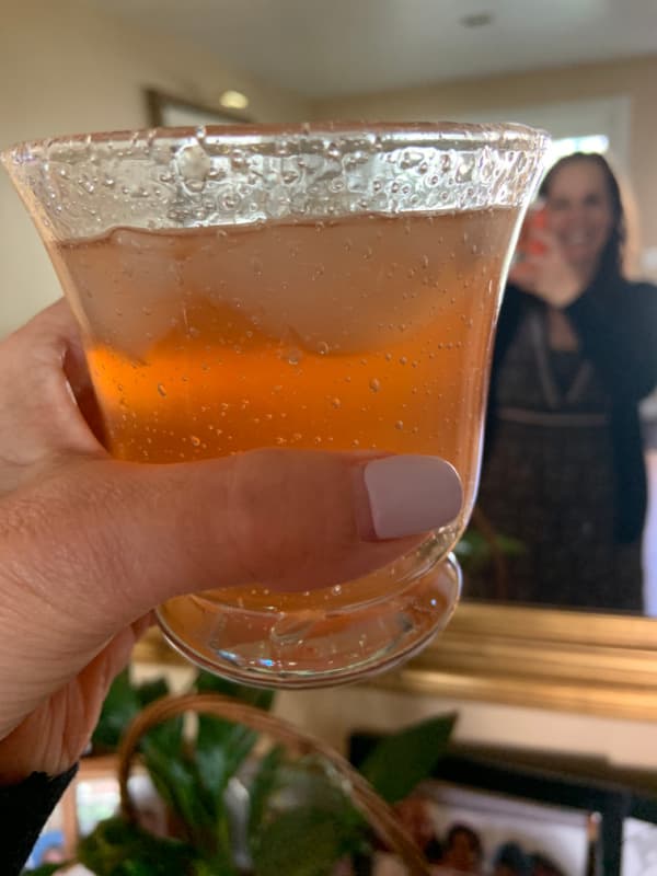 Woman toasting herself in the mirror with a pink drink.