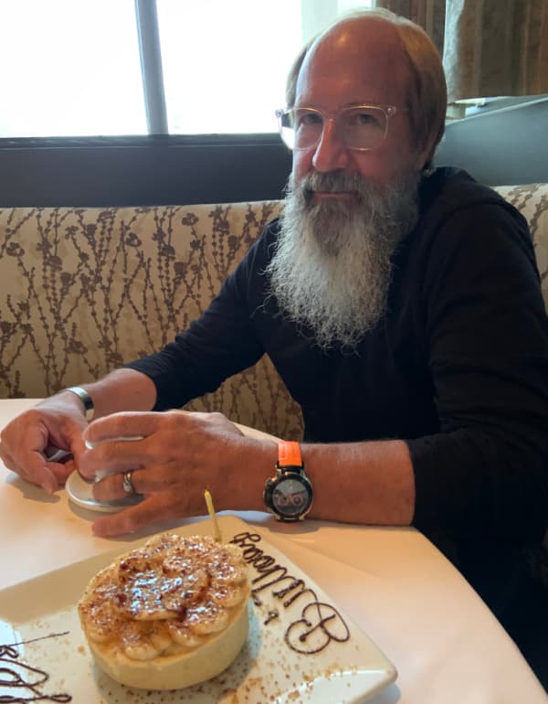 Bearded man with a banana pie with a candle in it.
