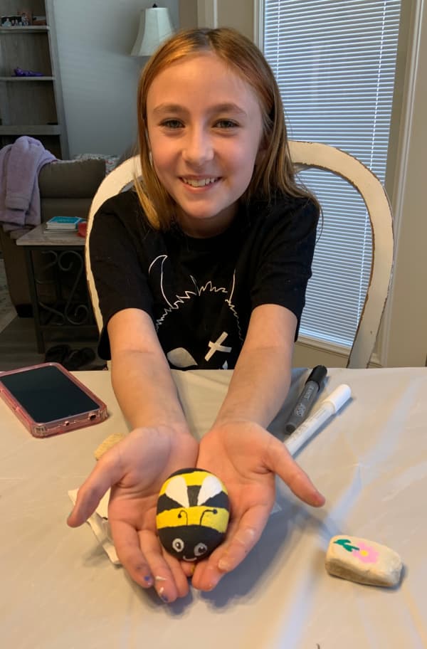 Girl holding a rock painted like a bee.
