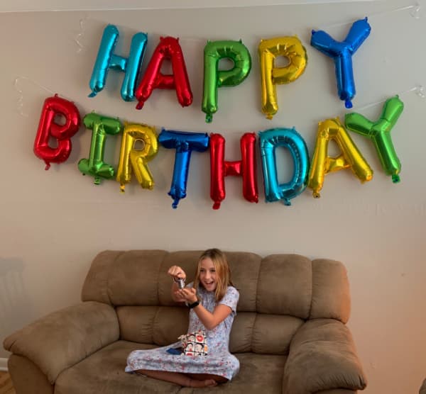 Young girls opening a gift under a Happy Birthday sign.