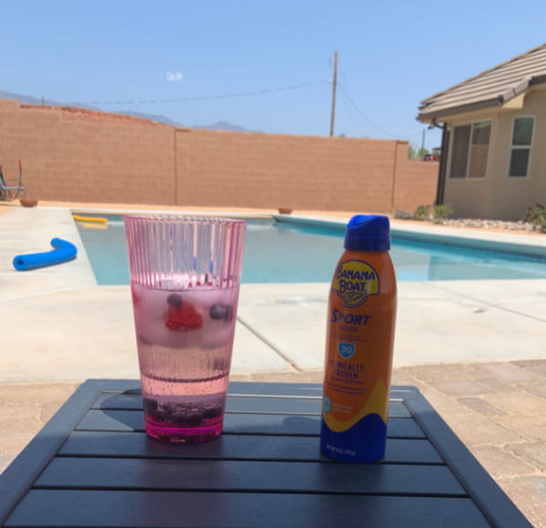 A berry drink and sunscreen in front of a swimming pool.
