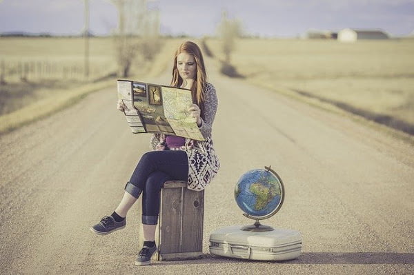 Woman in the road studying a map with a globe and a suitcase next to her.