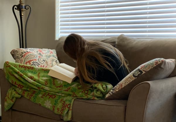 Teenage girl wrapped in a blanket, reading a book.