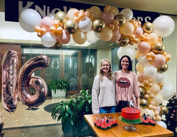Teenage girl and her mother with balloons and a birthday cake.