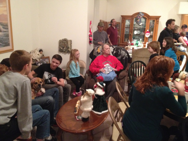Family crowded around watching Grandma open gifts.