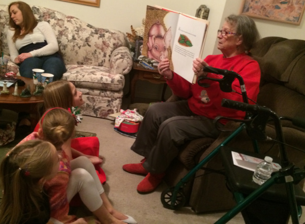 Grandmother in a Christmas sweater reading a book to the children. 
