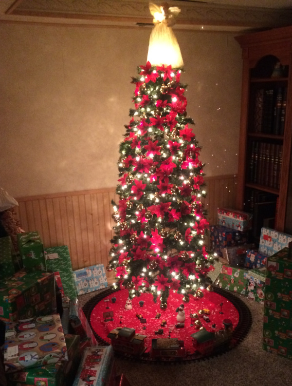 A lighted Christmas tree, with a train around the base and presents stacked on the sides.