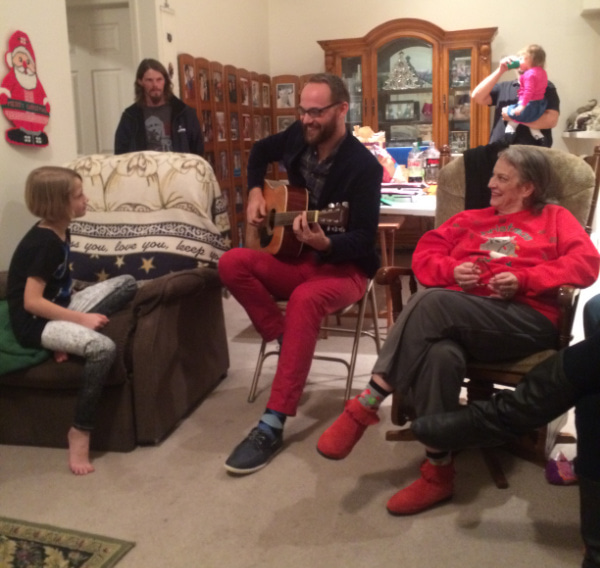 Young man playing the guitar surrounded by family.