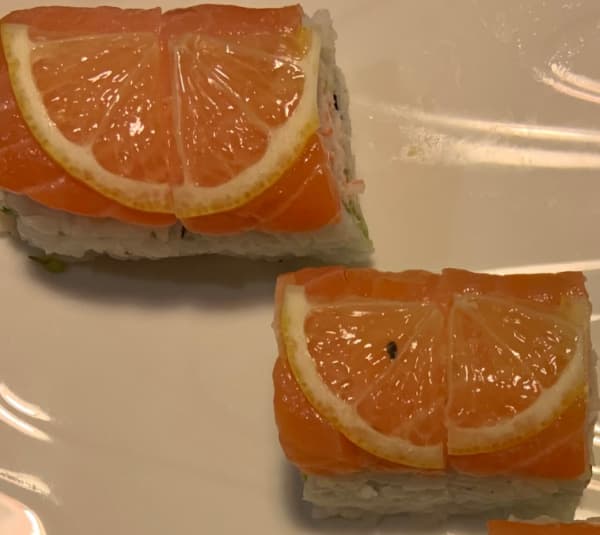 Two sushi rolls with salmon and lemon on top.