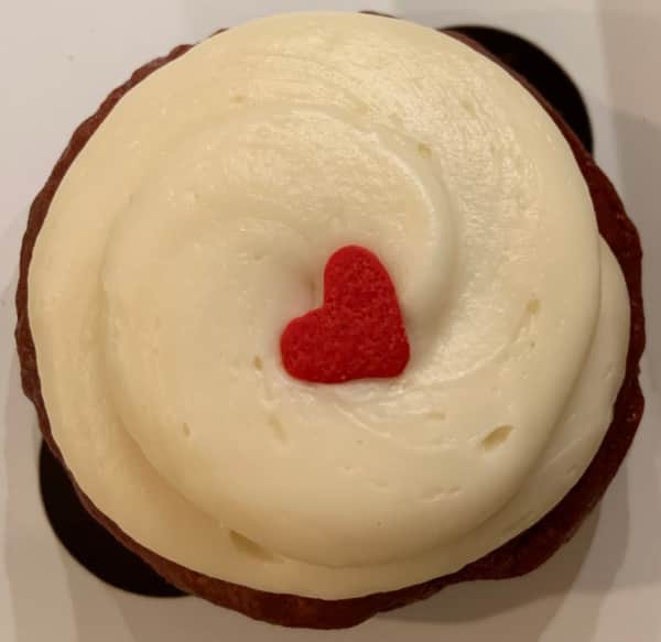 Red velvet cupcake with cream cheese frosting and heart-shaped candy.