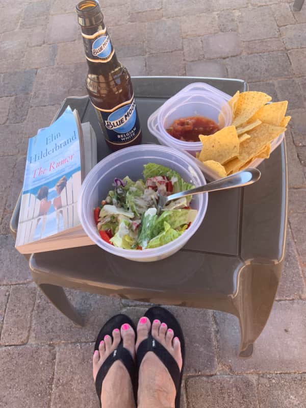 A book, a beer, a salad, chips and salsa, and feet in flip flops.