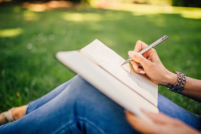 Woman sitting on the lawn writing in a notebook.
