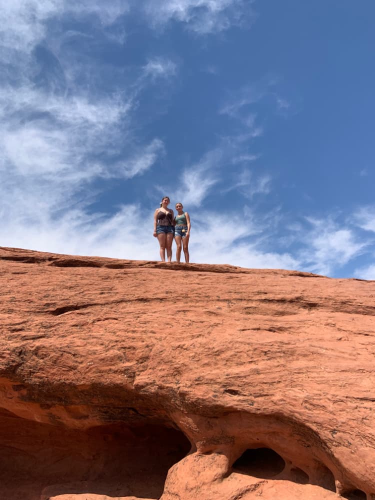 Two teenage girls standing on a large red rock.