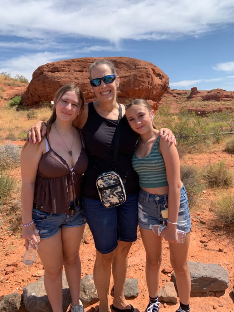 A grandmother and her two teenage granddaughters in front of a red rock.