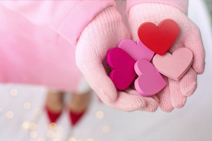 Gloved hands holding wooden hearts.