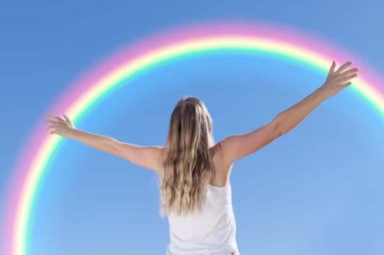 Woman holding up her arms in front of a rainbow.
