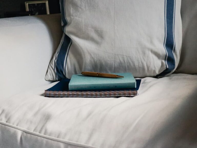 Journals and a pen on an overstuffed chair and pillow.