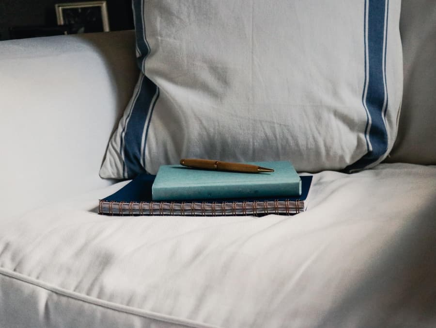 Journals and a pen on an overstuffed chair and pillow.