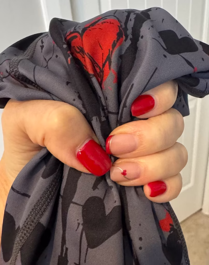 Woman's hand with Valentine nail art holding black and red leggings.