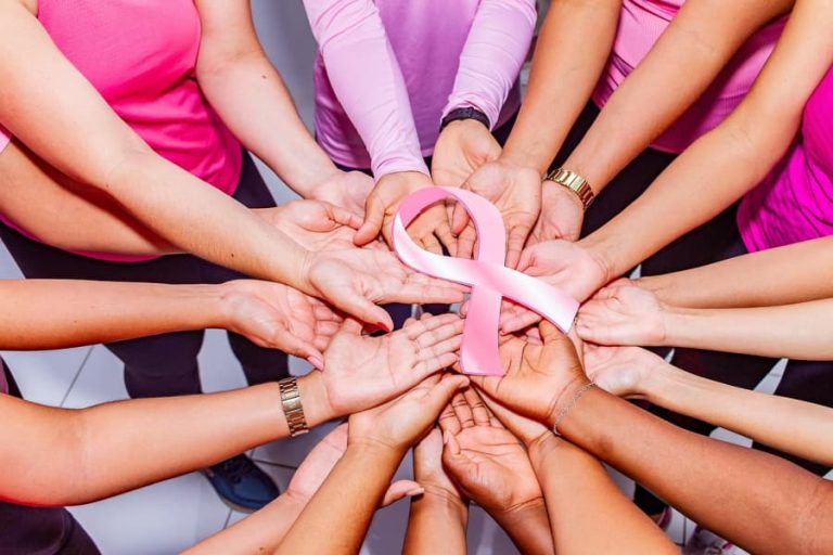 Women's hands holding a pink breast cancer awareness ribbon.