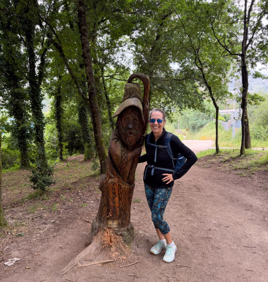 Woman standing next to a wooden sculpture of a pilgrim.
