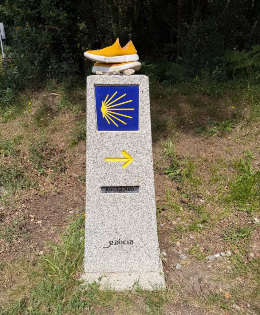 A Camino marker with yellow shoes on top of it.