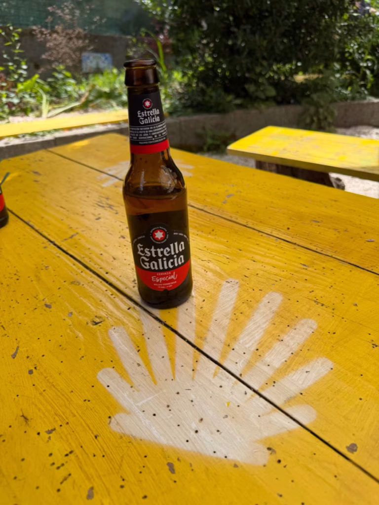 A beer on a yellow picnic table with a Camino shell painted on it.