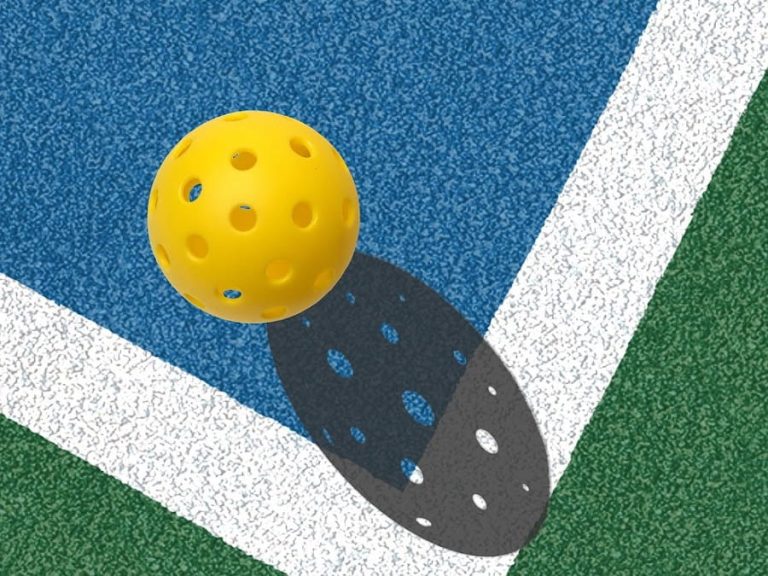 Yellow pickleball on a blue and green court.